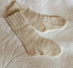 A pair of cream silk handmade baby's socks with seven rows of pattern and ribbing at the top.