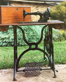 An antique black painted cast iron treadle sewing machine on a wooden base.