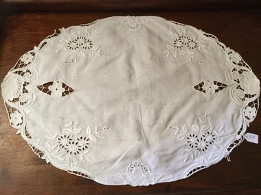 A large white oval cotton doiley with stitched edging, cutouts and embroidery.