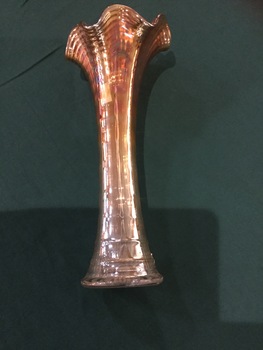 A narrow amber coloured carnival glass vase with a scalloped edge around the neck.