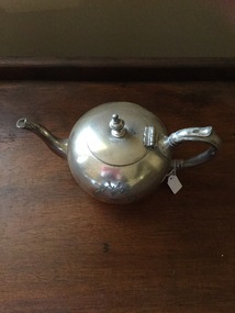 A sliver plated metal teapot with simple decoration and a dedication engraved on both sides.