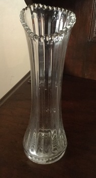 A tall clear glass vase with a vertical linear pattern and fluted edging.