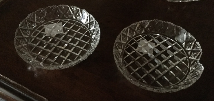 Two small round cut glass butter dishes with triangular pattern and scalloped edging.