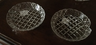 Two small round cut glass butter dishes with triangular pattern and scalloped edging.