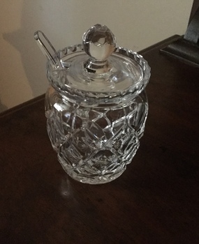 A cut glass diamond patterned sugar bowl with a lid and two glass spoons.