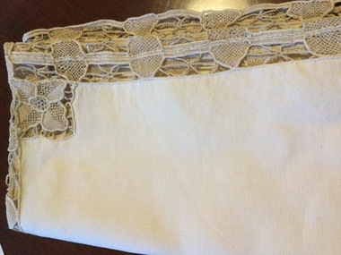 A cream coloured small square tablecloth with embroidered edge and centre panels.