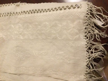 A long white patterned cotton table runner, which has two lines of open stitched pattern down the middle.