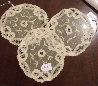 Three small round ecru coloured lacy pattered doilies with a scalloped edge.