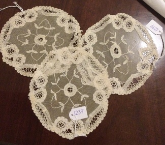 Three small round ecru coloured lacy pattered doilies with a scalloped edge.