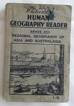 Grey paperback Whitcomb'e Human Geography Reader for Grade VIII with a picture of a city next to a river with wharf activity on the opposite side of the river. The cover is worn and ink stained with Lance Sebire written at the top.