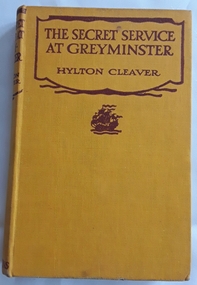 A yellow hardcover book for boys with the title written in brown lettering,The Secret Service at Greyminster, author Hylton Cleaver along with a picture of a galleon underneath. 