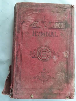 The red cloth badly damaged hymnal has black and gold faded lettering of title and symbol of E surrounded by a circle on the front cover.