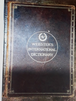 A maroon leather covered International Dictionary Australasian Edition with gold lettering for the title on the front cover. Has A-M written in small gold letters down the right side of the cover which is detached from the spine.
