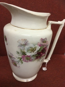 Large white porcelain bedroom jug with pink and white flowers as well as gold trim.