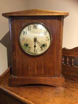 Plain wooden mantle clock with a ceramic dial, black digits and hands. Has a glass cover that opens.