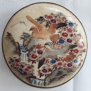 A hand painted Japanese style ladies belt buckle with flowers, waterfalls, and birds with a mountain in the background.