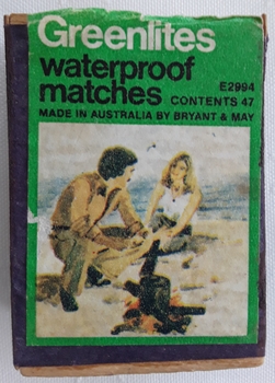 A matchbox and waterproof safety matches with a picture of two people near a fire on the beach.