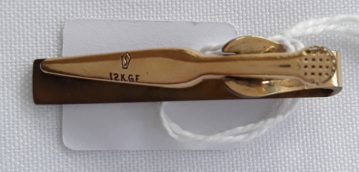 A gold plated tiepin with some engraving on the top and bottom.