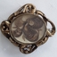 A swirled patterned highly decorated brass brooch with human hair under a glass cover.