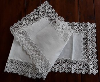 A long white floral patterned lace embroidered edged cotton table runner for a table or sideboard.