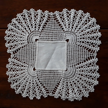 A square cotton handmade scallop edged doiley for use on furniture to protect the surface.