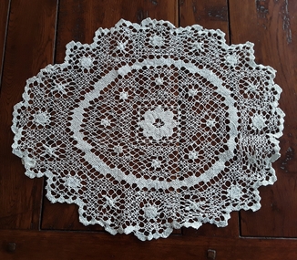 A large open patterned white crotched doiley with a scalloped edge used for protecting furniture.