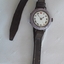 A purple CYMA ladies watch with roman numerals and a brown leather watchband in its case.