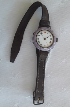 A purple CYMA ladies watch with roman numerals and a brown leather watchband in its case.