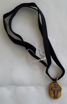 An oval gold locket with 12 coral stones mounted on a raised cross with hair inside. It has a black velvet ribbon.