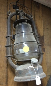 A rusty tin and glass "hurricane" lamp for used for lighting outside.