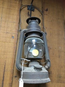 An early 20th century kerosene lamp for outdoor use with a metal frame and glass chimney.