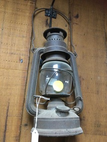 An early 20th century kerosene lamp for outdoor use with a metal frame and glass chimney.