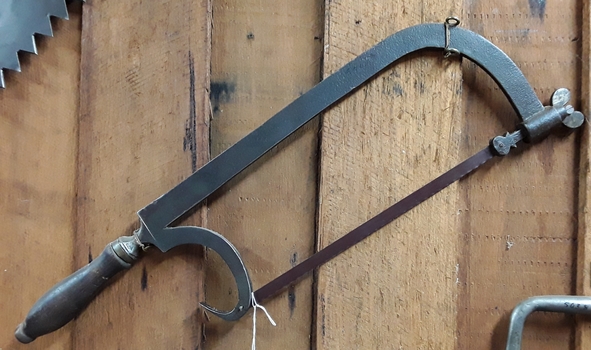 A steel bow saw with a nail puller and saw blade attached.