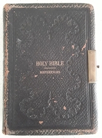 A small faded black covered Holy Bible with a damaged brass hinge.
