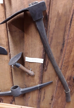A forged steel adze with a curved wooden handle used to shape wood.