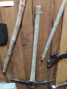 A two pointed steel handmade pick with a wooden handle used to break up soil.