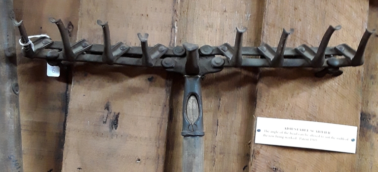 A hand used steel adjustable scarifier with a long wooden handle.