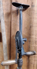 A manual steel breast drill with a flat plate at the top and two wooden handles.