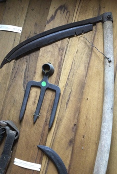 A handmade curved double bladed metal scythe with a long curved wooden handle.