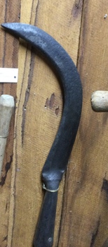 A handmade slasher with a long wooden handle and a heavy sharp steel blade attached with a rivet to the handle. 