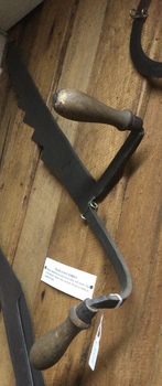 A silage or hay knife with two turned wooden handles. The blade has eight teeth.