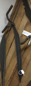 A steel curved double bladed silage or hay knife with two wooden handles at the top attached by rivets. 