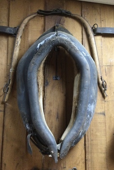 A pair of handmade wooden horse hames which are linked together by a leather strap at the top.