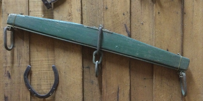 A wide flat green painted wooden triangular shaped swingletree with a steel bar attached under the wooden section.