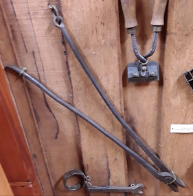 A pair of long handled vintage handmade blacksmith tongs with two handles which are riveted together to form a hinge joint for the flat edged tongs.