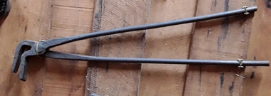 A pair of vintage handmade blacksmith tongs with two handles riveted together forming a hinge joint for the 90 degree right angled flat tongs.