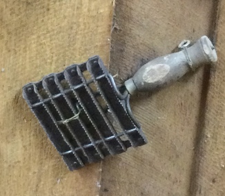A vintage handmade metal horse curry comb with a turned wooden handle used for grooming horses.