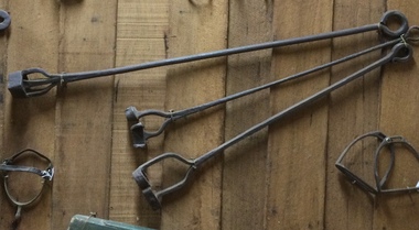 A vintage steel branding iron with two prongs with the brand H S on one end and a ring at the other end.