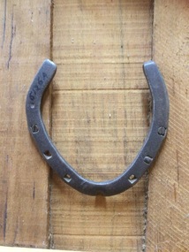 An iron curved horseshoe with three square shaped holes on each side for nails.