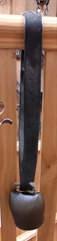 A brass cowbell with a brass striker and a handle at the top for the wide black leather strap to go through.